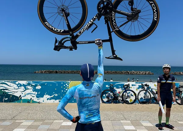 海辺で自転車を頭上に掲げるメンバー